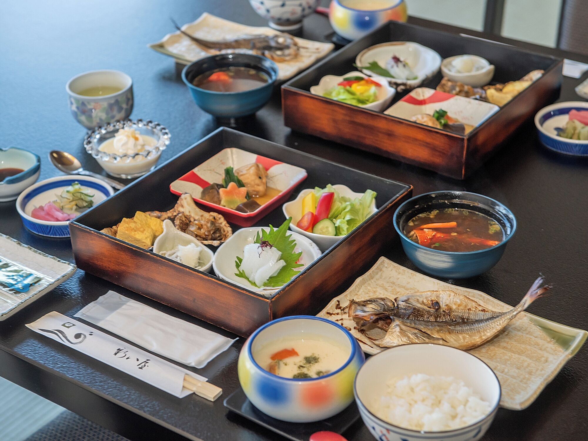 A variety of dishes arranged on a table, including bowls of soup, plates of fish, and other food items.