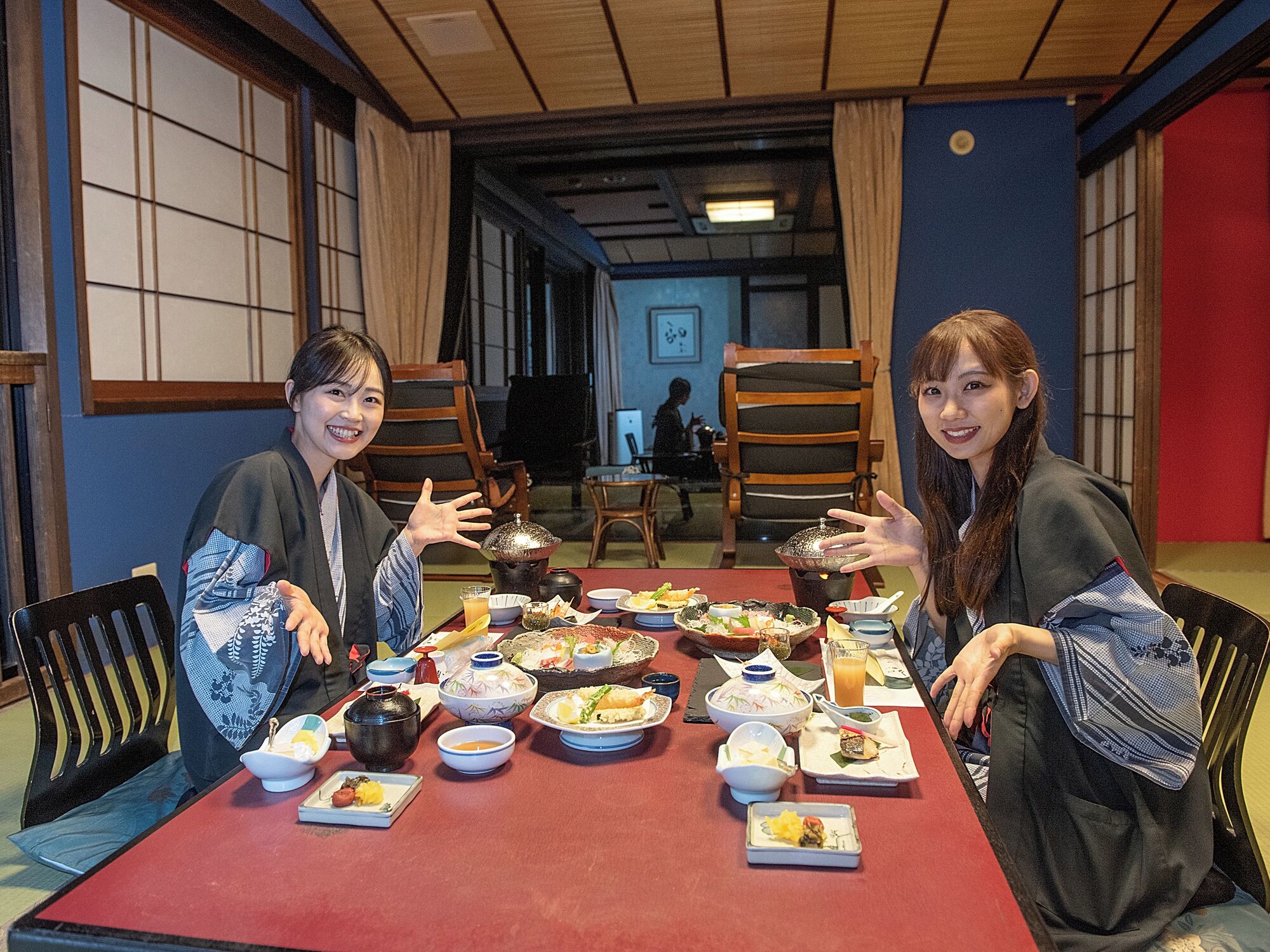A traditional Japanese room with tatami mat flooring, wooden sliding doors, and a low table with various dishes.