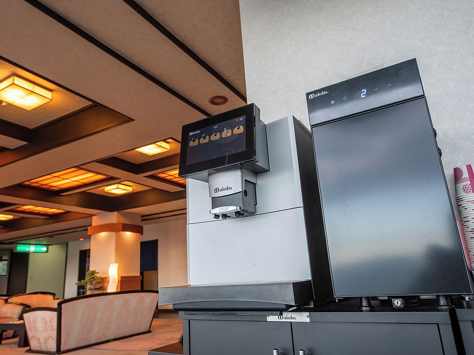 A modern hotel lobby with a Daihols coffee machine and a refrigerator.