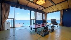 A room with tatami flooring, a table with chairs, a heater, and large windows offering a view of the sea. - Shinpachiya (Toba)