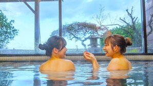 Two people in a hot spring bath with a view of trees and a building through large windows. - Shinpachiya (Toba)