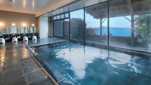 A modern indoor swimming pool with clear glass walls, a wooden ceiling, and a view of the sea. - Shinpachiya (Toba)