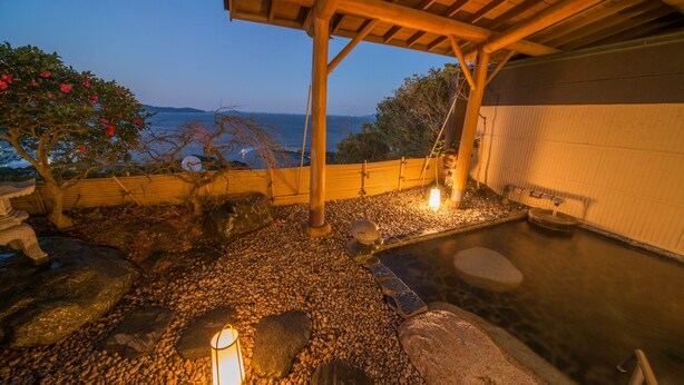 A traditional Japanese onsen with a wooden structure, a stone hot spring, and a view of the sea. - Shinpachiya (Toba)