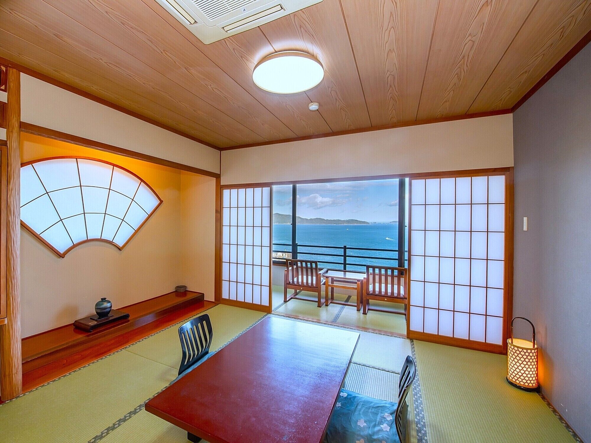 Una habitación japonesa tradicional con suelo de tatami, una mesa de madera baja y vista al mar a través de biombos shoji.