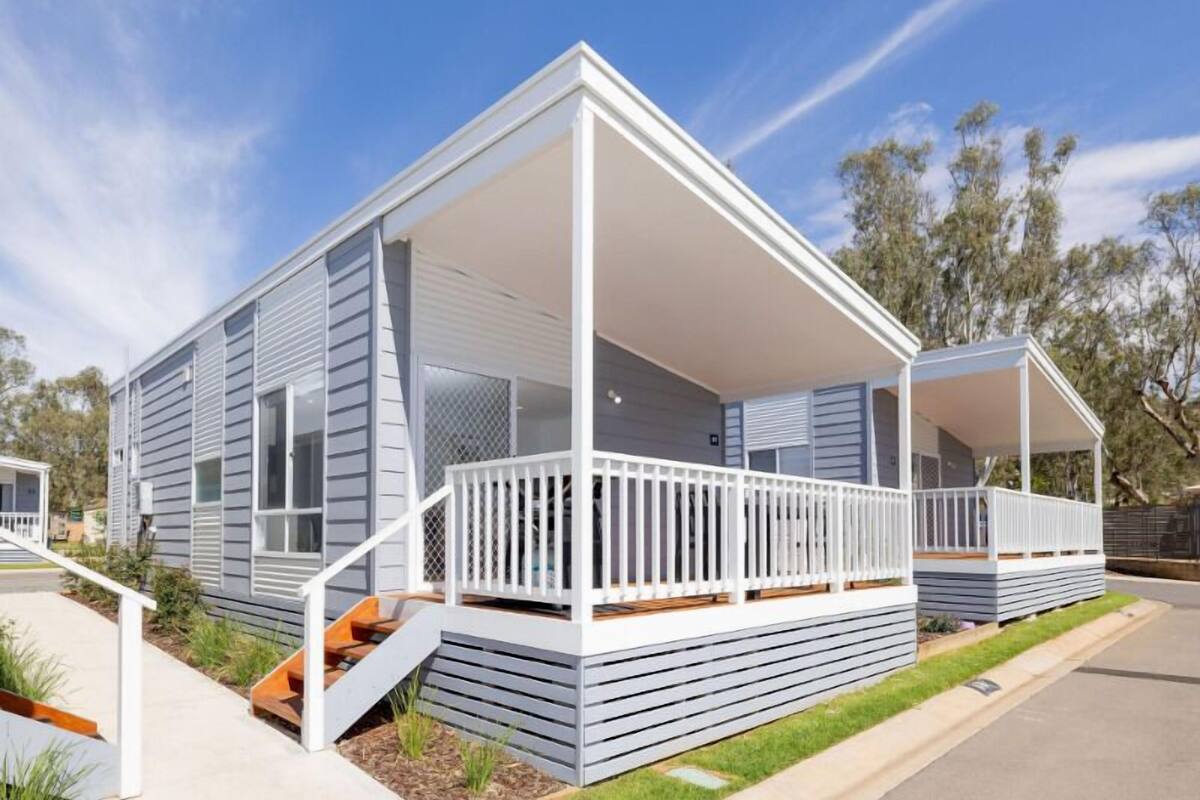 A modern mobile home with a covered porch, a small deck, and a front yard.