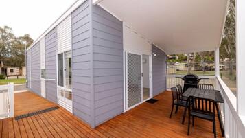 A covered outdoor area with a wooden deck, a grill, and a table with chairs.