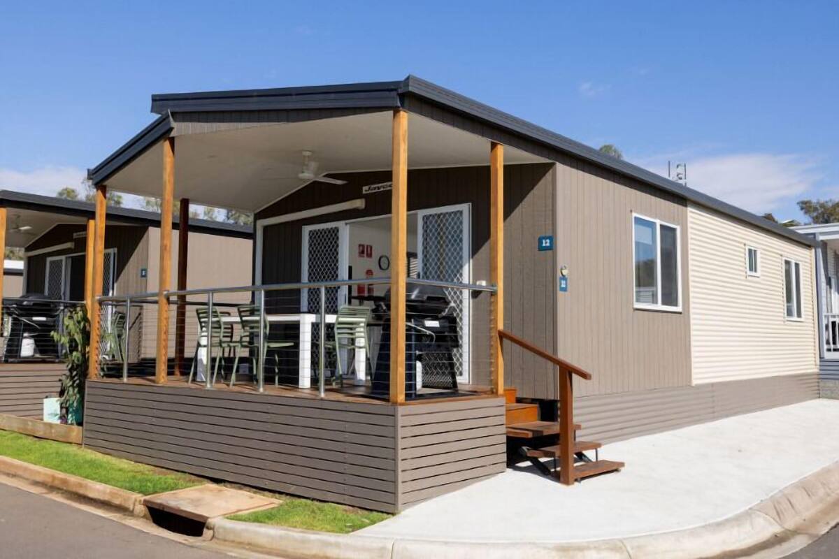 A single-story mobile home with a covered porch, a small deck, and a fenced outdoor area with tables and chairs.
