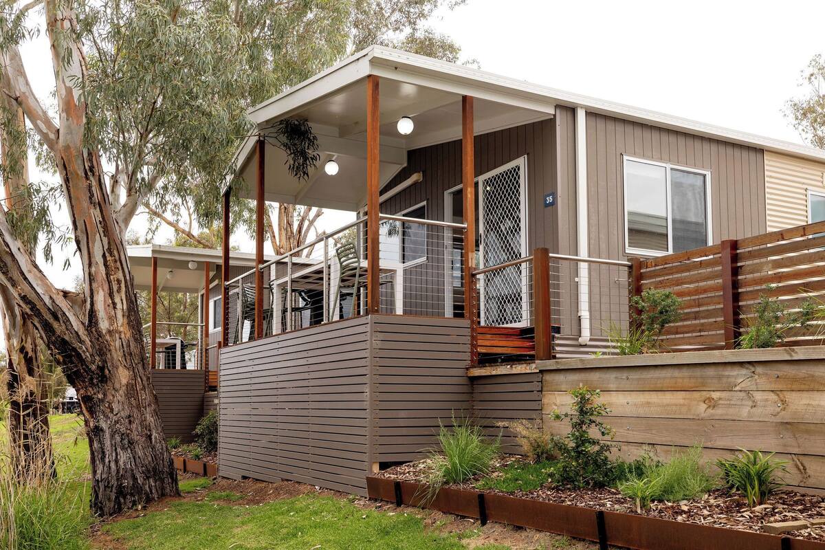 A modern house with a covered porch, a fenced garden, and a large tree.