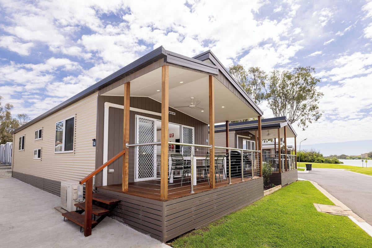 A single-story mobile home with a covered porch, a small outdoor seating area, and a grassy lawn.