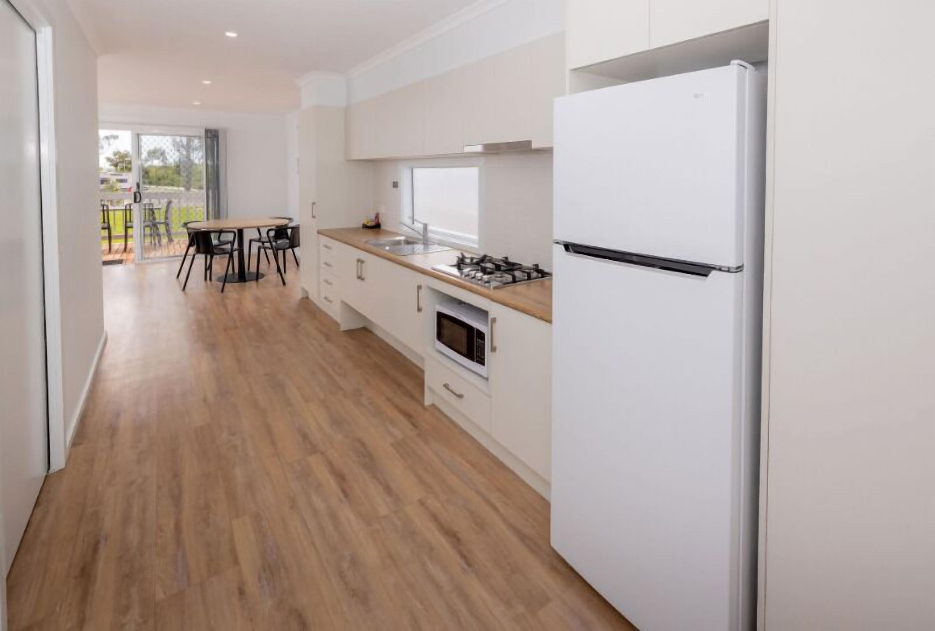 Una cocina moderna con un refrigerador blanco, una estufa a gas y un microondas. Hay un comedor con una mesa y sillas.