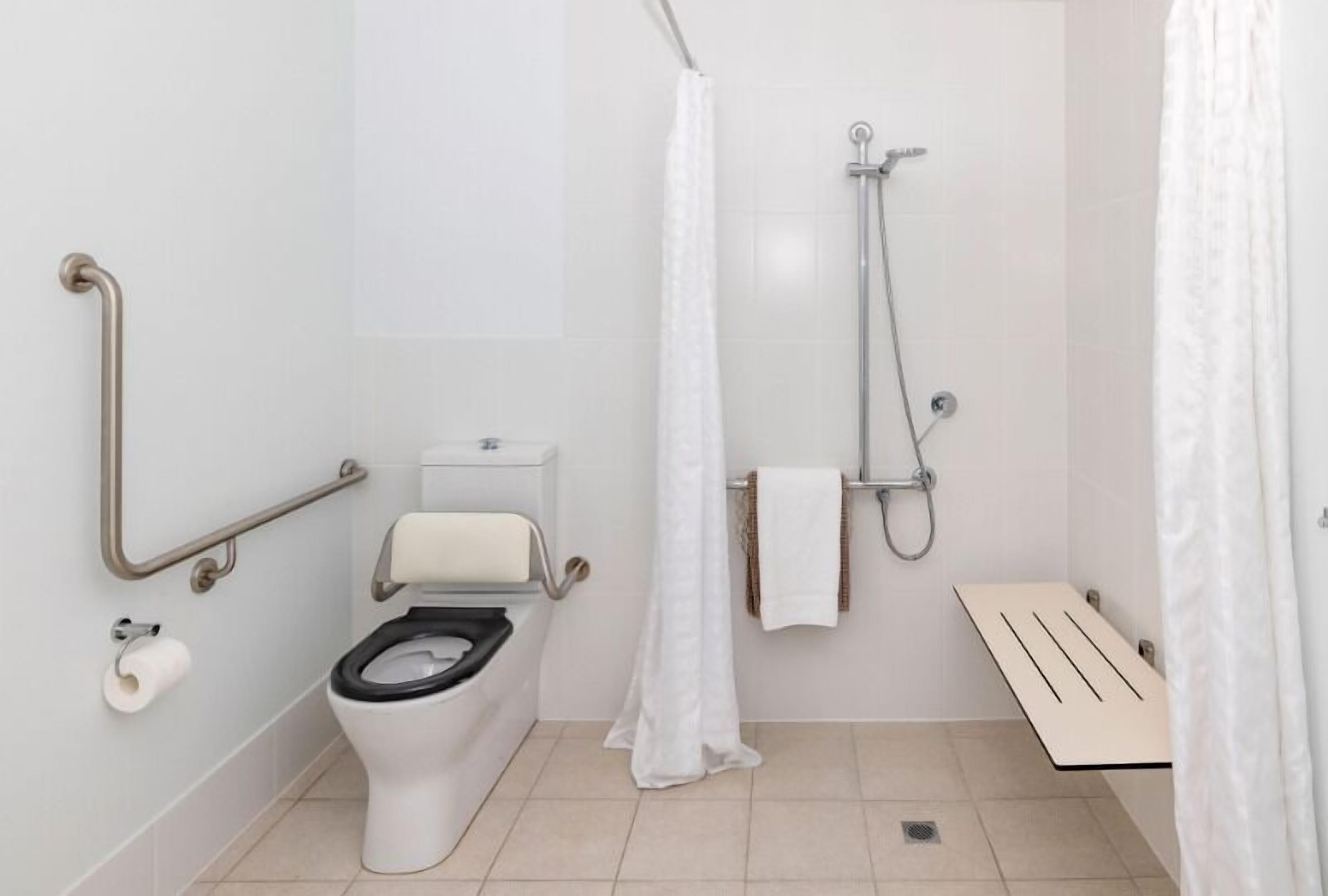 A modern bathroom with a toilet, shower, and grab bars.