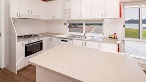 A modern kitchen with white cabinets, a large island, a gas stove, and a view of a lake through a window. - BIG4 Mannum Holiday Park (Mannum)