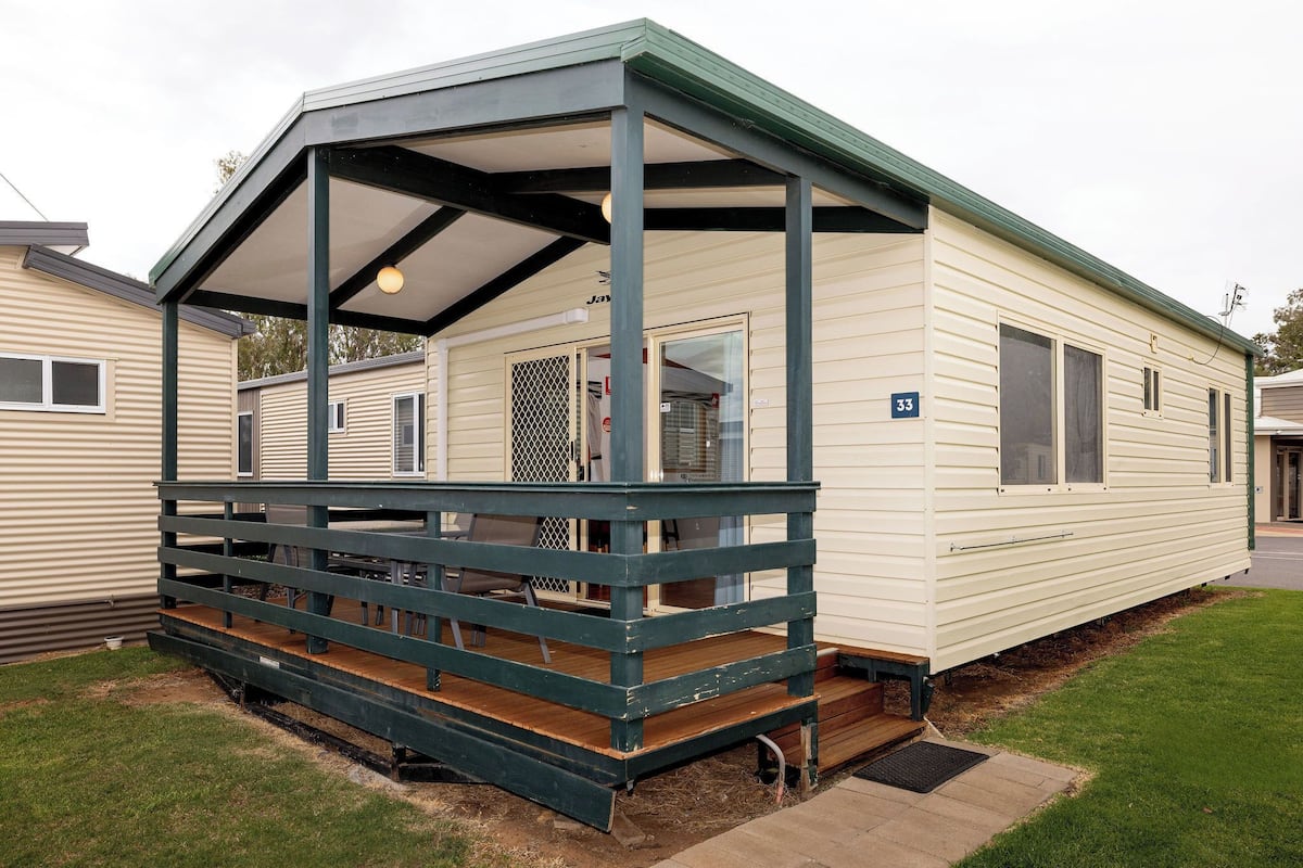 A mobile home with a covered porch, a number '33' sign, and a small front yard.