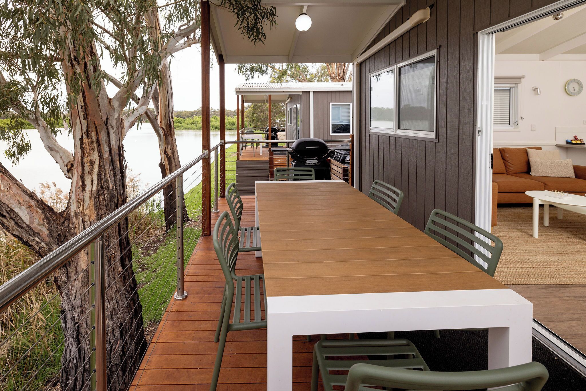A covered deck with a table and chairs, a barbecue grill, and a view of a lake.