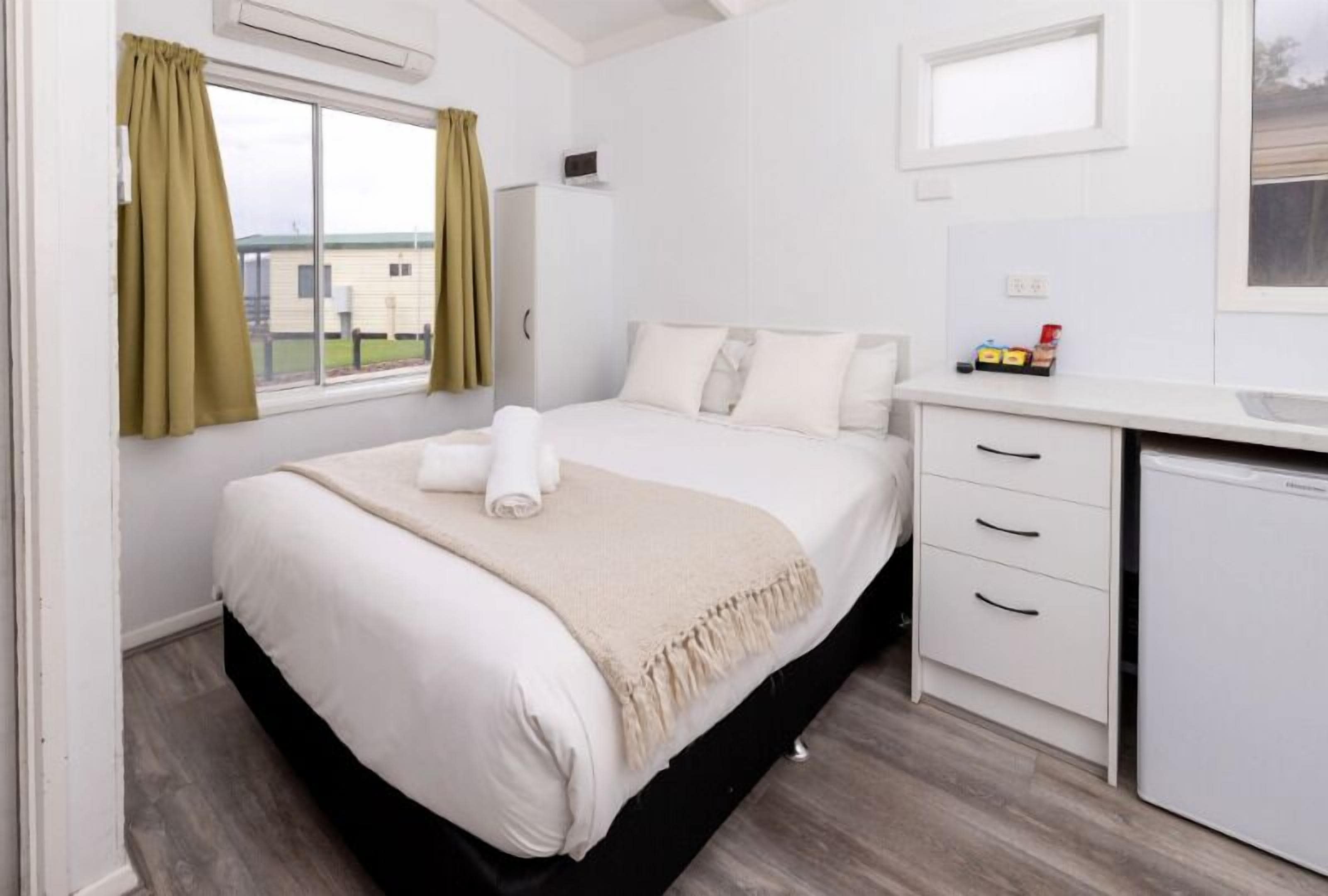 Une chambre à coucher avec un lit, une table de chevet, un bureau et une fenêtre avec des rideaux.