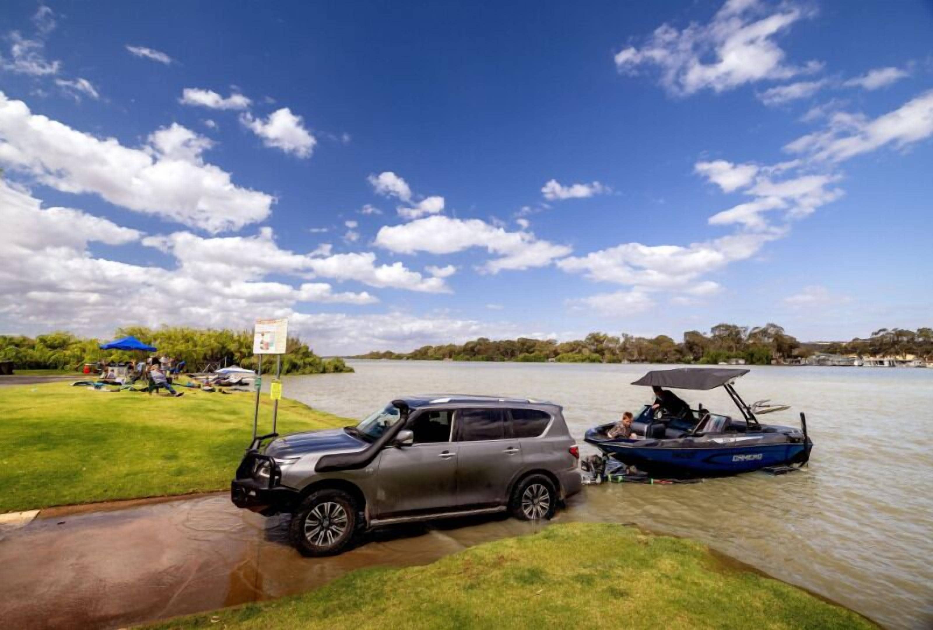 A car parked by a lake with a boat nearby.