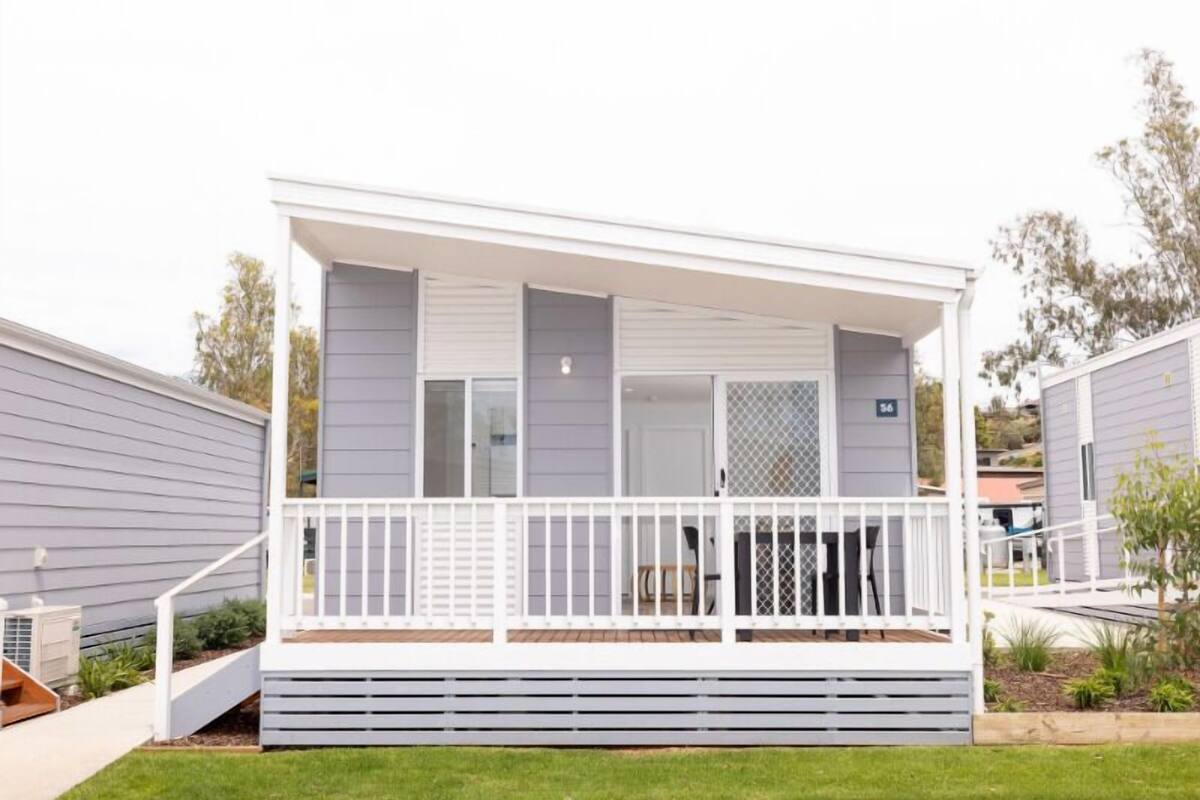 A two-story mobile home with a covered porch and a small deck area.