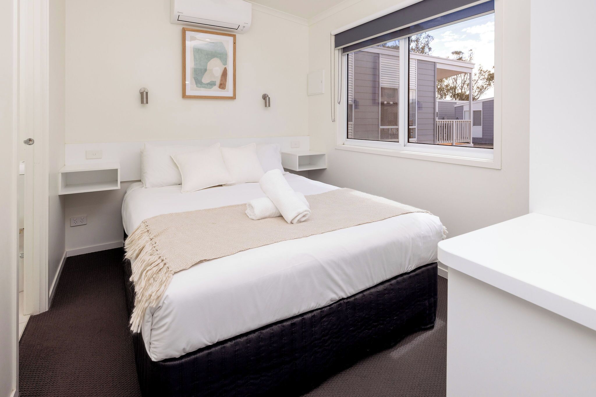 A neatly arranged bedroom with a bed, bedside tables, a window, and a view of the outside.