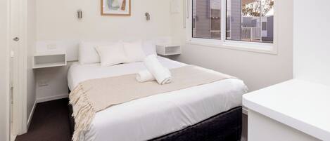 A neatly arranged bedroom with a bed, bedside tables, a window, and a view of the outside.