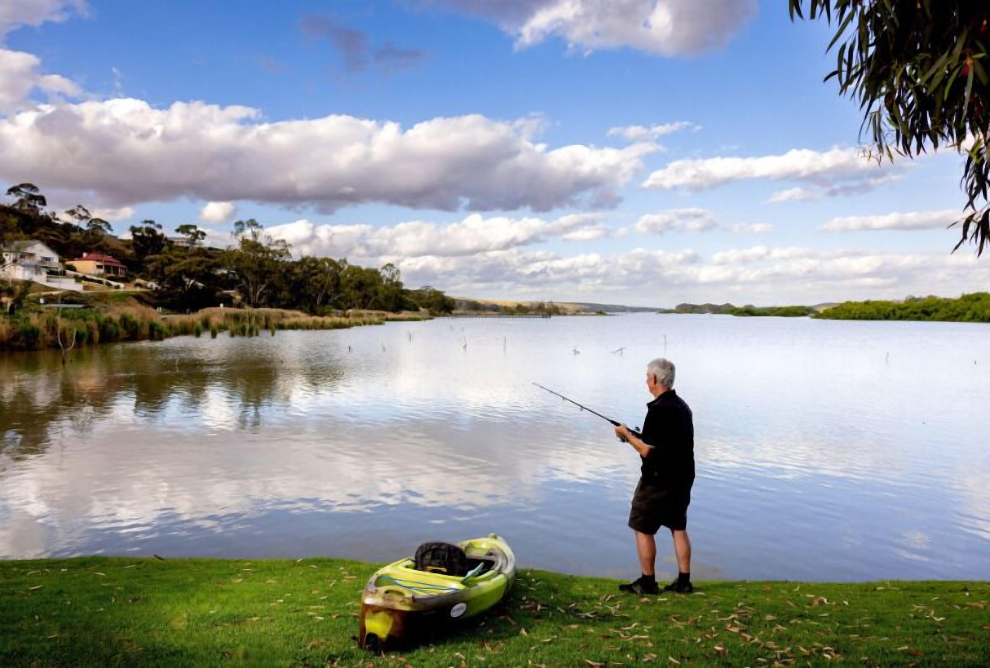 A person fishing by a calm lake with a small boat nearby.