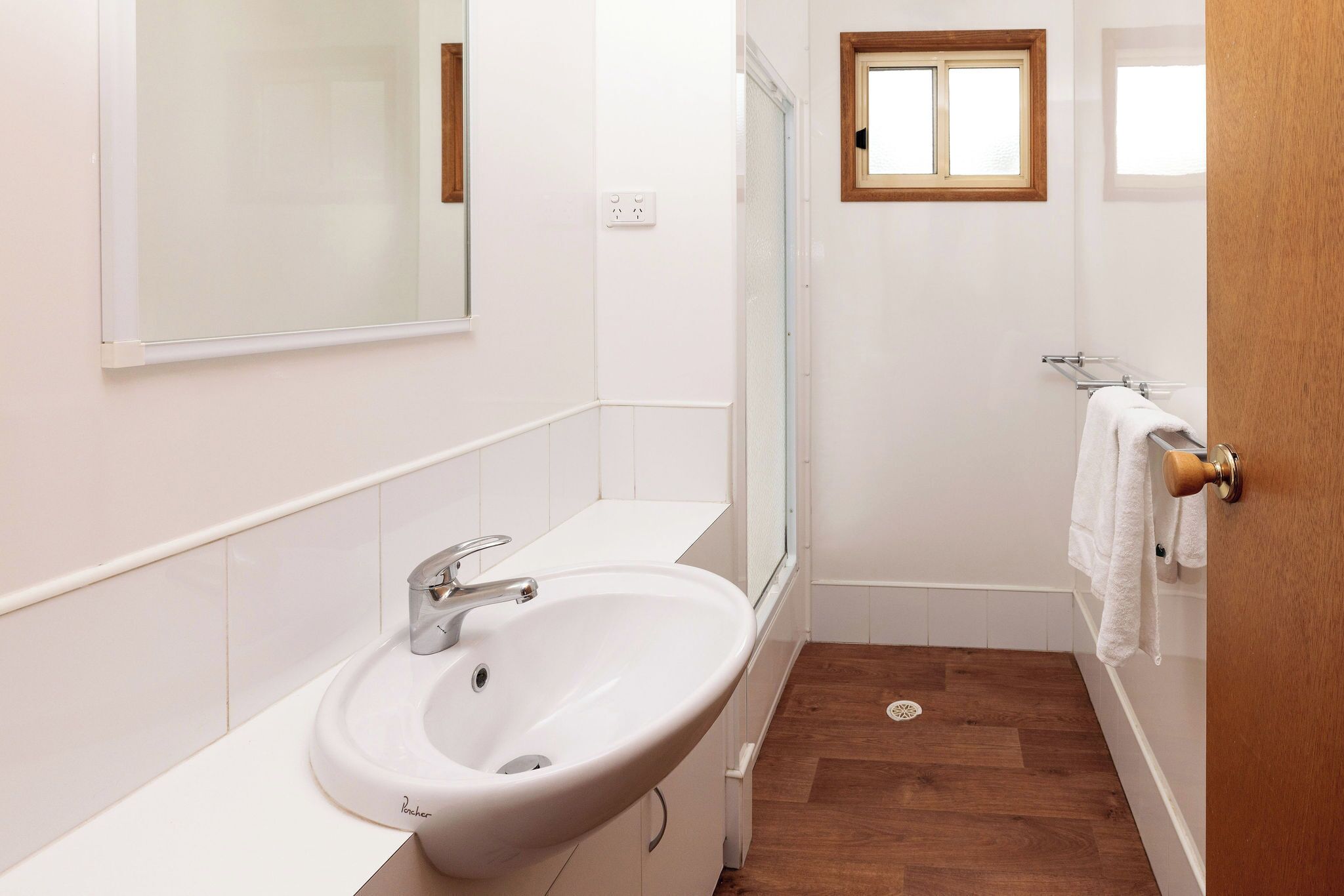 Un baño con lavamanos blanco, espejo y suelo de madera.