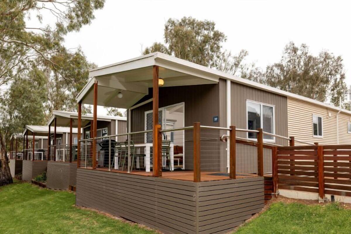 A mobile home with a covered porch, a fenced deck, and a grassy yard.
