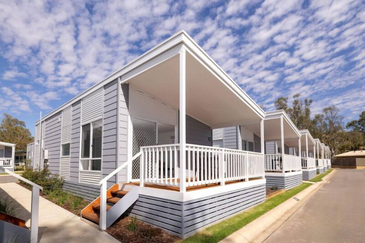 A row of modern mobile homes with white exteriors and wooden decks, featuring a simple, functional design.