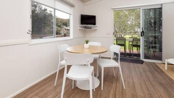 A modern room with a round wooden table, white chairs, a mounted TV, and a sliding glass door leading to an outdoor area.