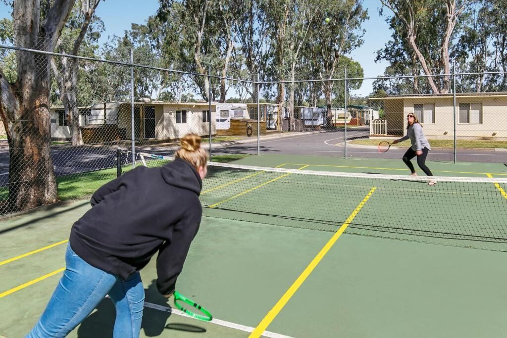 An outdoor tennis court with a net, surrounded by trees and a fence.