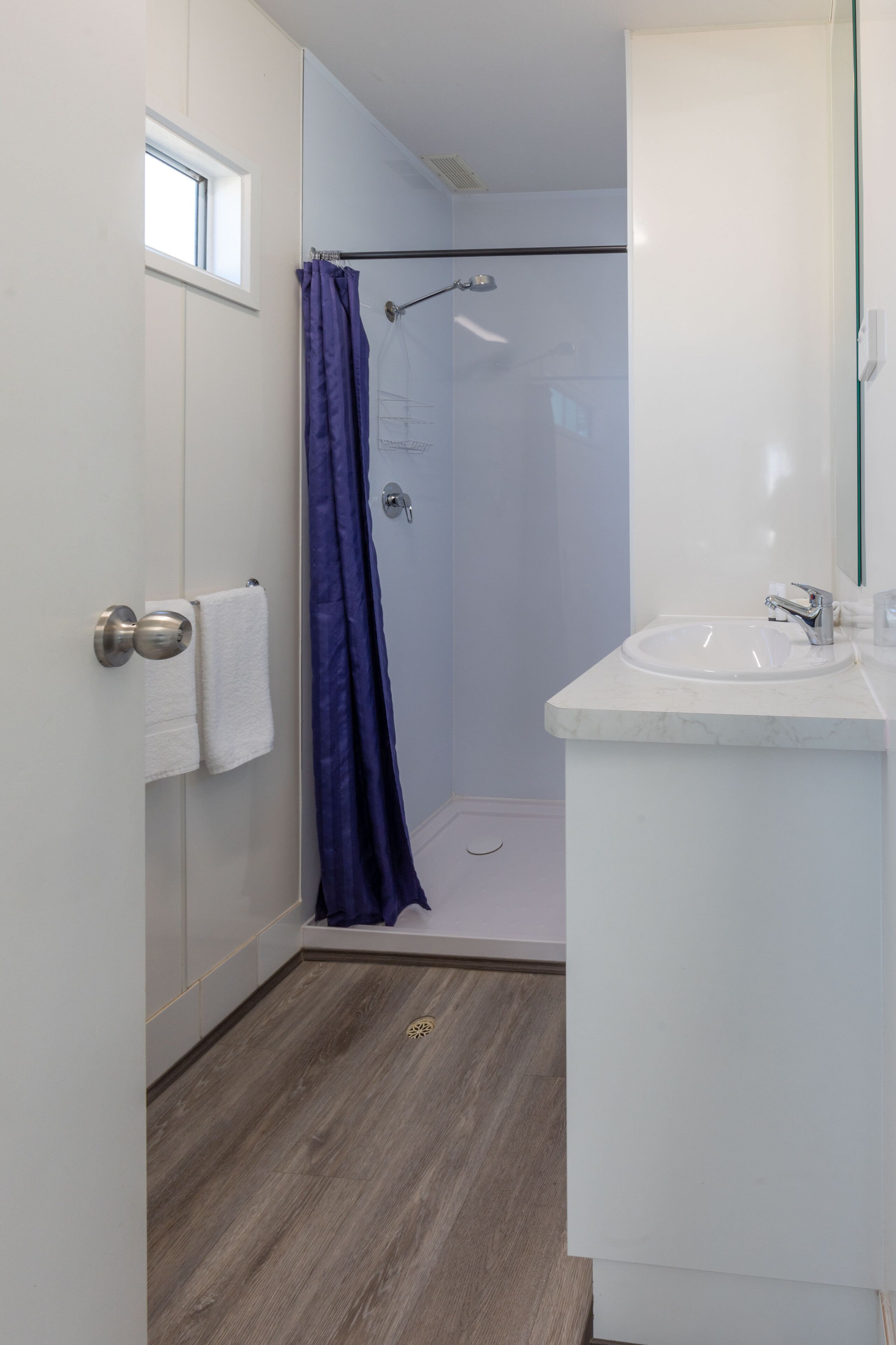 Un baño con ducha, lavamanos y un perchero para toallas.