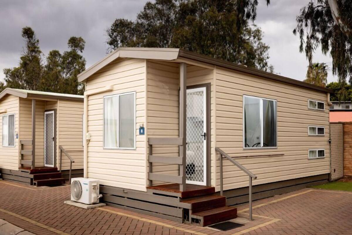 A mobile home with a front porch, a small set of stairs, and a single air conditioning unit.