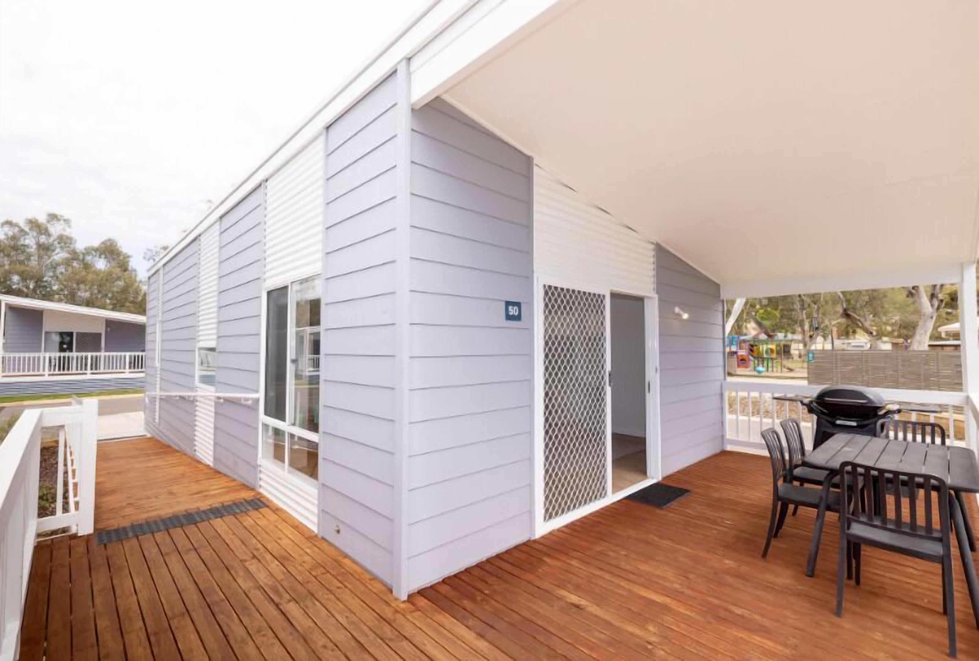 A covered outdoor area with a wooden deck, a barbecue grill, and a seating area with chairs and a table.
