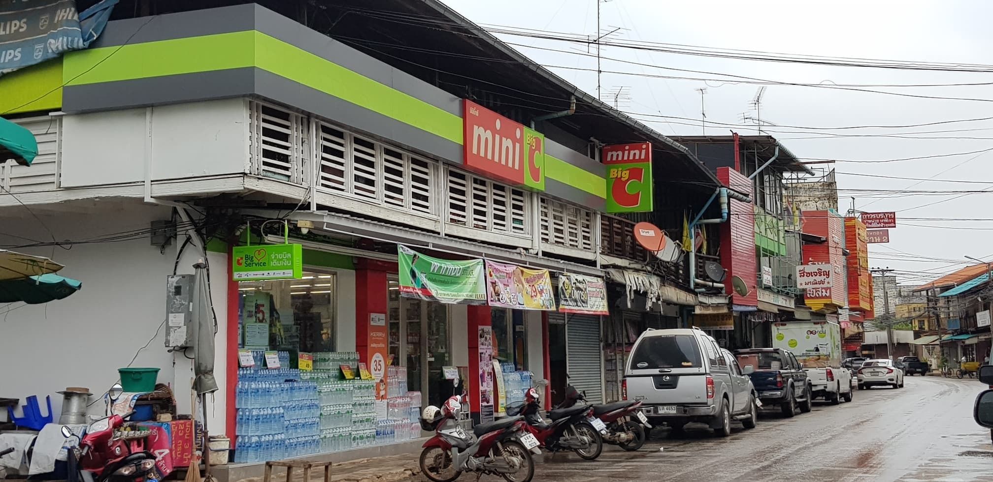 A street with various shops, including a pharmacy and a mini Big C store.