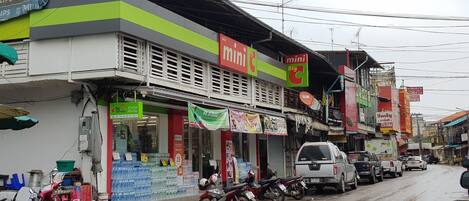 A street with various shops, including a pharmacy and a mini Big C store.