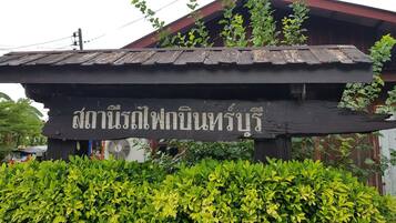 Ein hölzernes Schild mit thailändischen Schriftzeichen, einem roten Dach und grünem Laub davor.