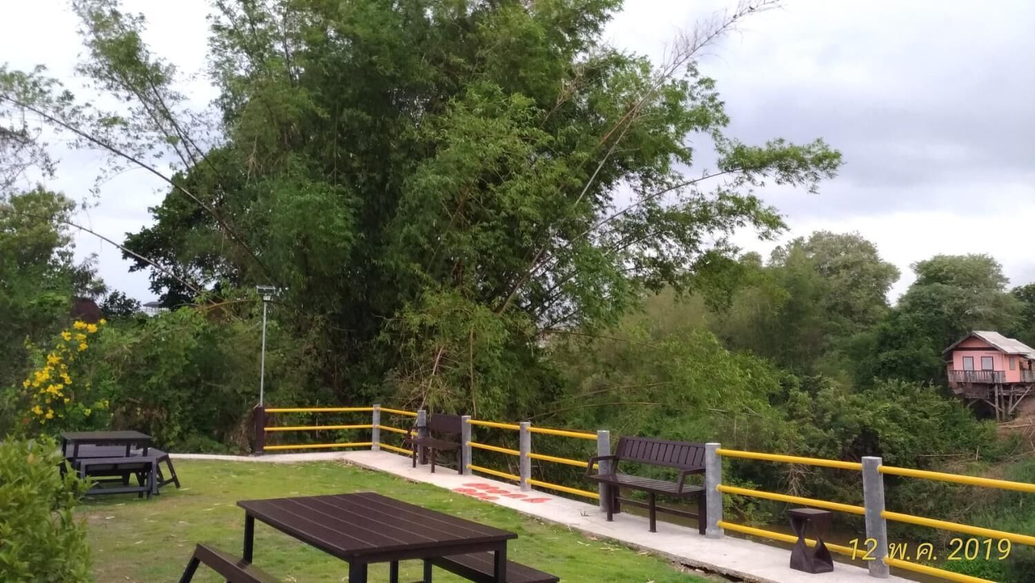 Een picknickplaats met tafels en banken, omringd door een gele balustrade, en een grote boom op de achtergrond.