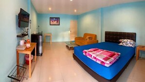 A bedroom with a bed, a TV, a desk, a chair, and a door. - Baansri Family (Kabin Buri)