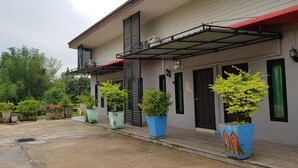 A building with a covered outdoor area, potted plants, and a gated entrance. - Baansri Family (Kabin Buri)