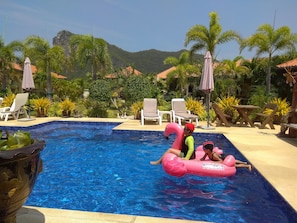 A swimming pool with lounge chairs and umbrellas, surrounded by greenery and a mountainous backdrop. - Stella Resort (Sam Roi Yot)