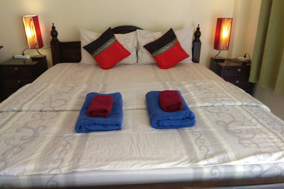 A neatly made bed with a patterned bedspread, two red towels, and two red and black pillows.