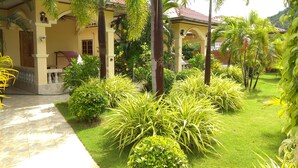 A well-maintained garden with palm trees and manicured lawns in front of a yellow building with a tiled roof. - Stella Resort (Sam Roi Yot)