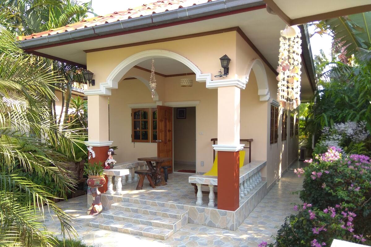 A covered porch with a stone floor, a wooden table, and chairs.