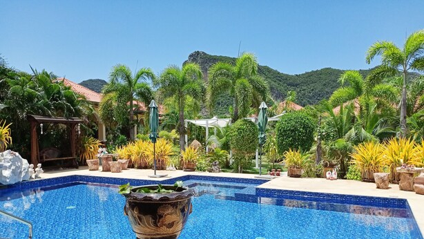A swimming pool with a decorative urn, surrounded by tropical plants and a view of a mountain. - Stella Resort (Sam Roi Yot)