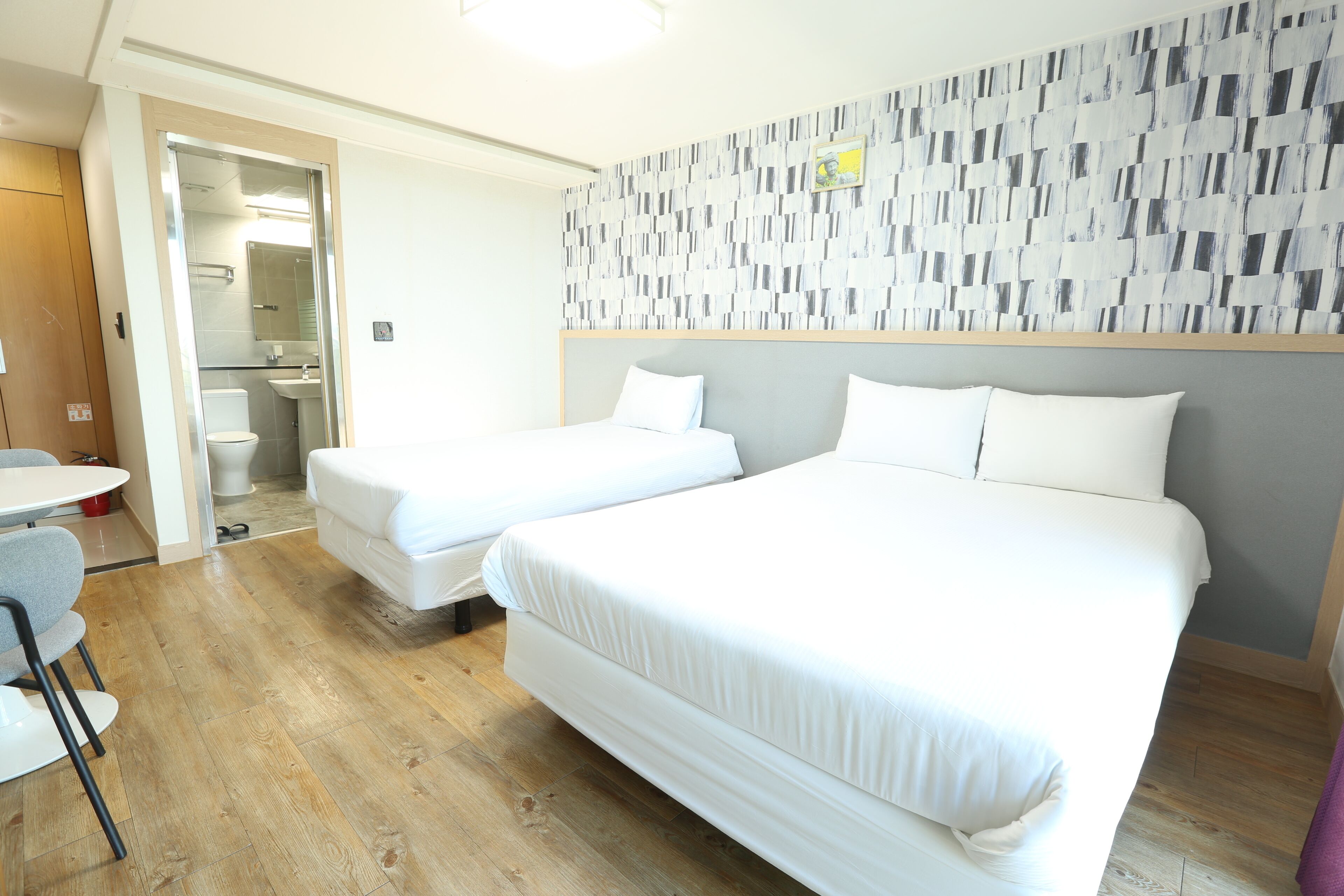 Habitación de hotel con dos camas, una mesita pequeña y un baño visible a través de una puerta abierta.
