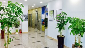 A clean, well-lit hallway with potted plants, a fire extinguisher, and artwork on the walls. - Jeju Moseulpo Hotel (Seogwipo)