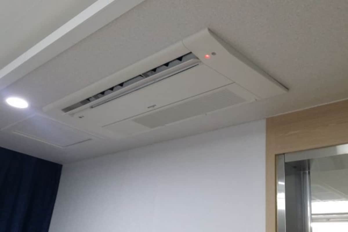 A ceiling-mounted air conditioning unit in a room with white walls and a wooden trim.