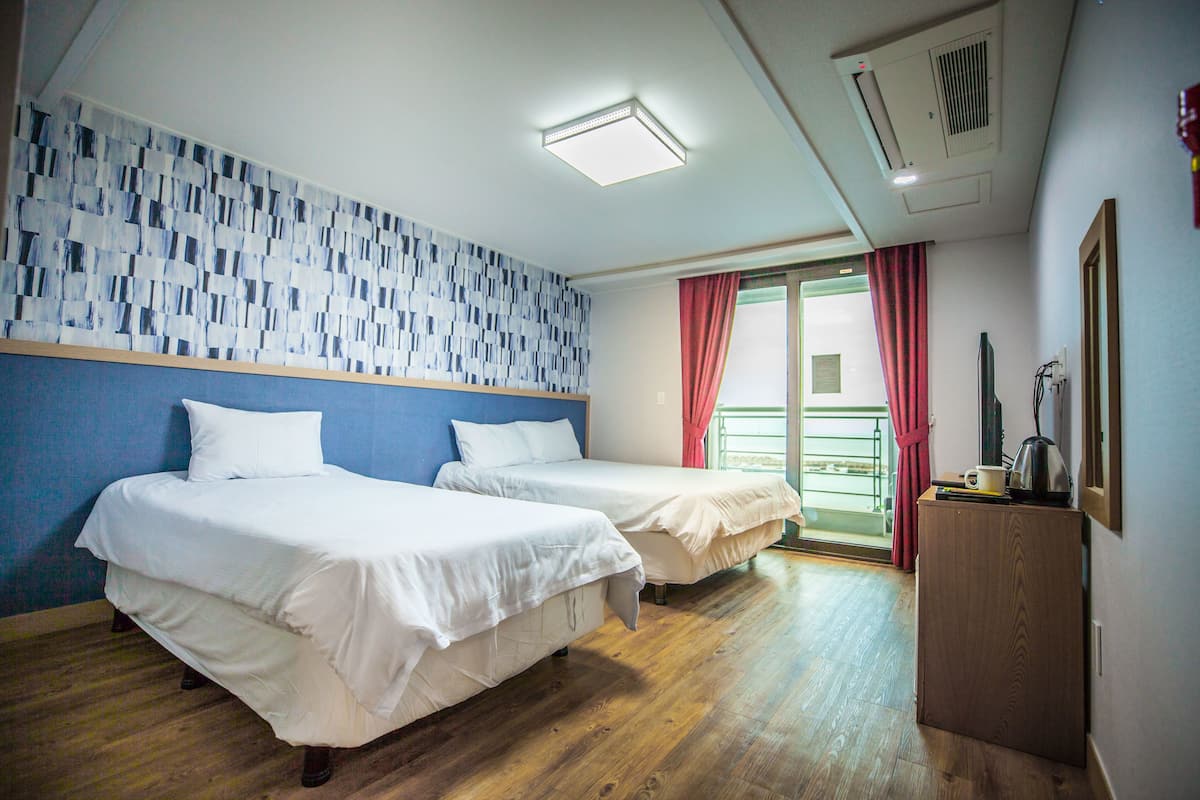 Ein Hotelzimmer mit zwei Einzelbetten, Holzboden, Wand mit Muster und einem kleinen Schreibtisch mit Wasserkocher.