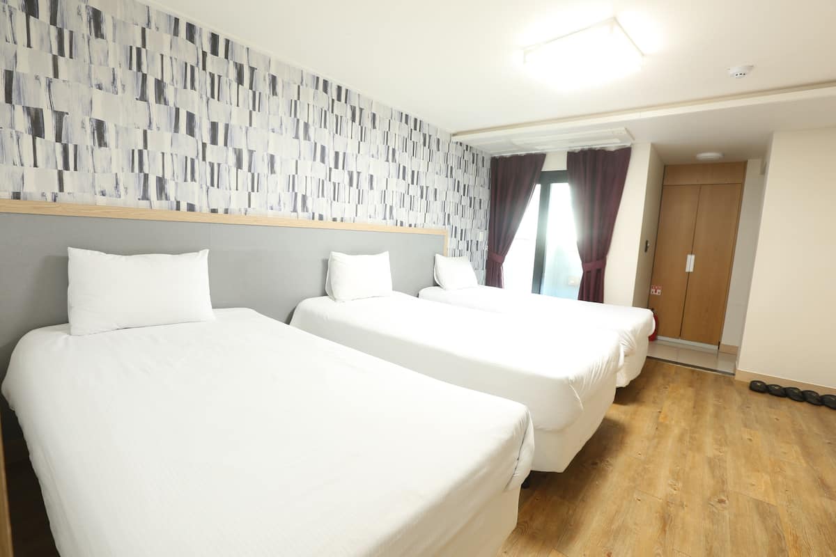 Ein Hotelzimmer mit drei Einzelbetten, Holzboden und einer Wand mit Muster.