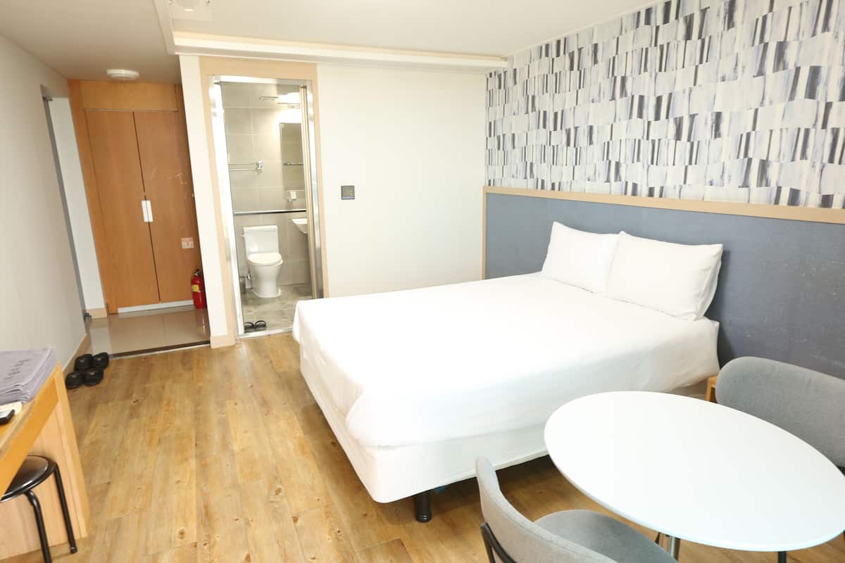 Ein Hotelzimmer mit Bett, einem kleinen Tisch, einem Stuhl, einem Kleiderschrank und einer Dusche.