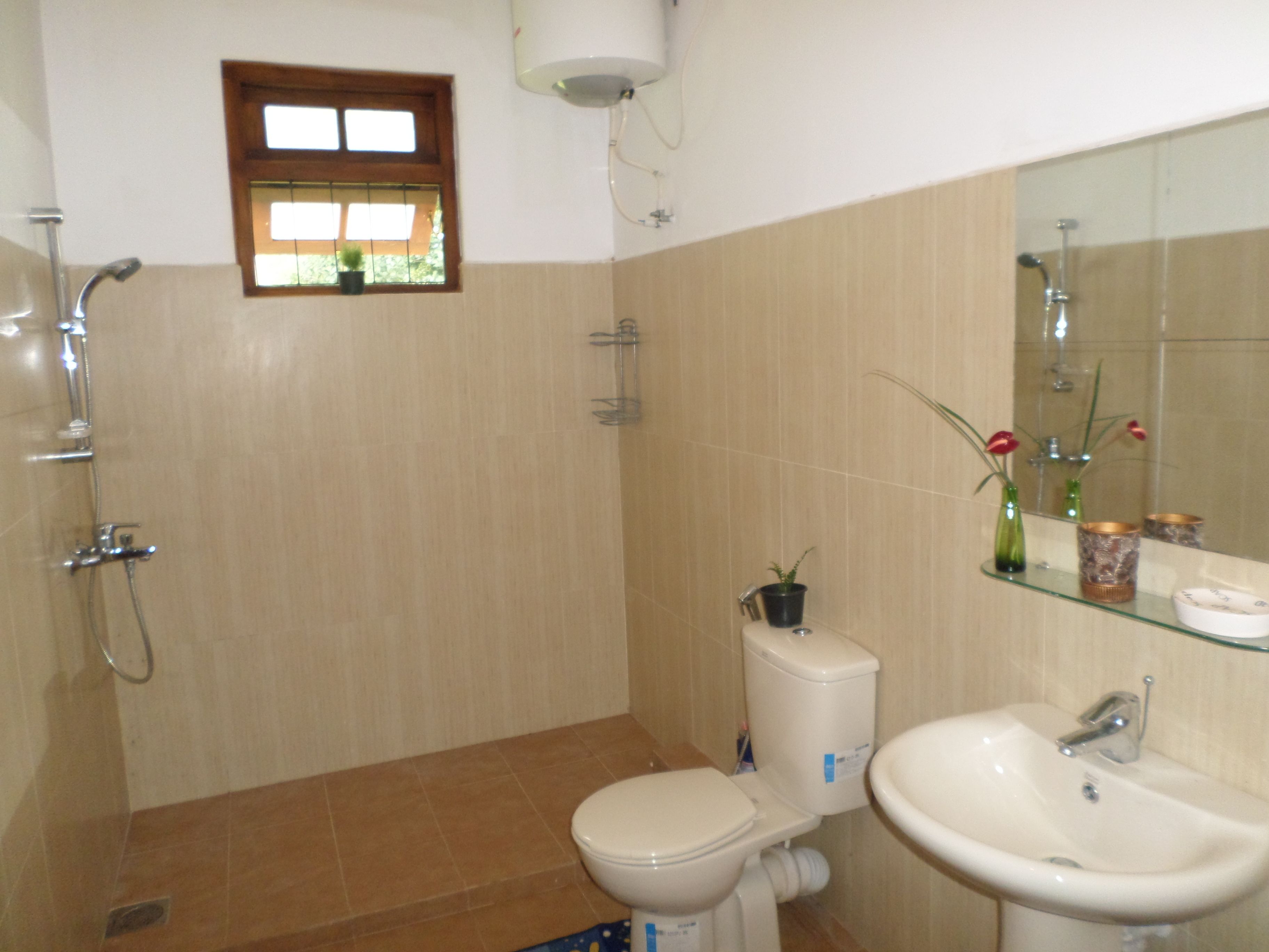 A bathroom with a toilet, bidet, sink, and a window with a view of greenery.